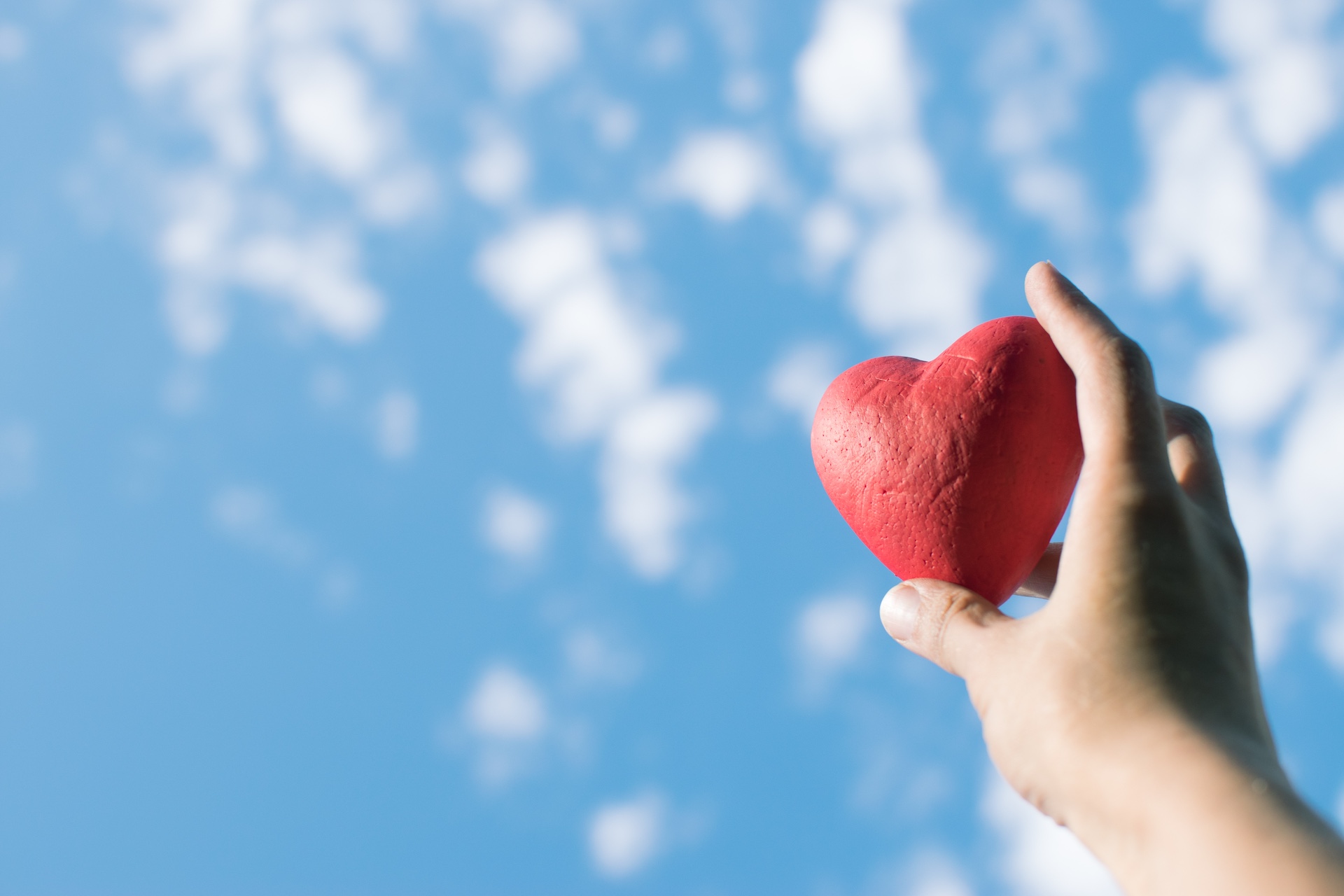 Hand holding the red decorative heart against the blue sky. Day of donor. Love concept